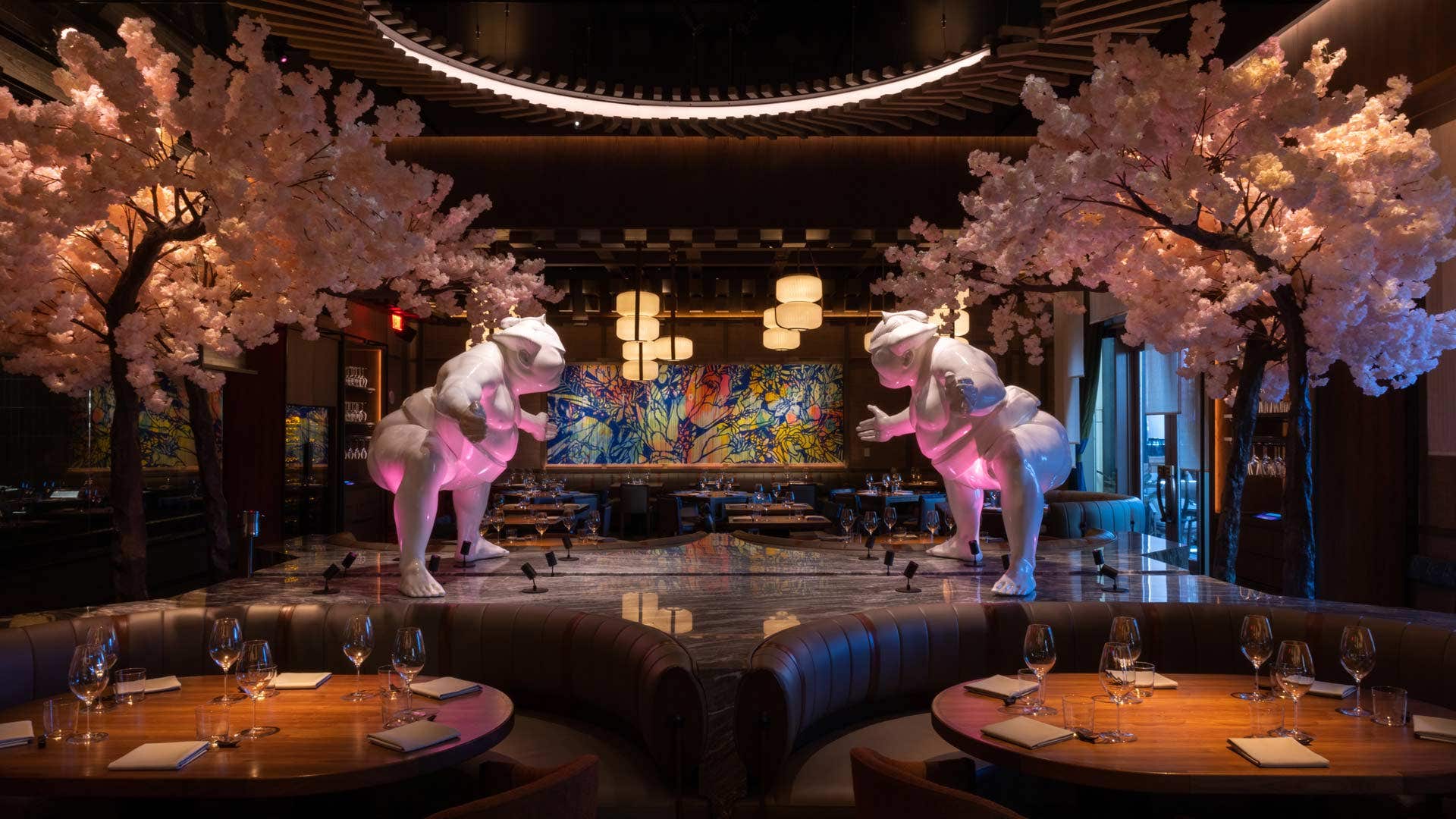 A stylish restaurant with two white sculptures and cherry blossom trees, soft pink lighting, and elegant table settings.