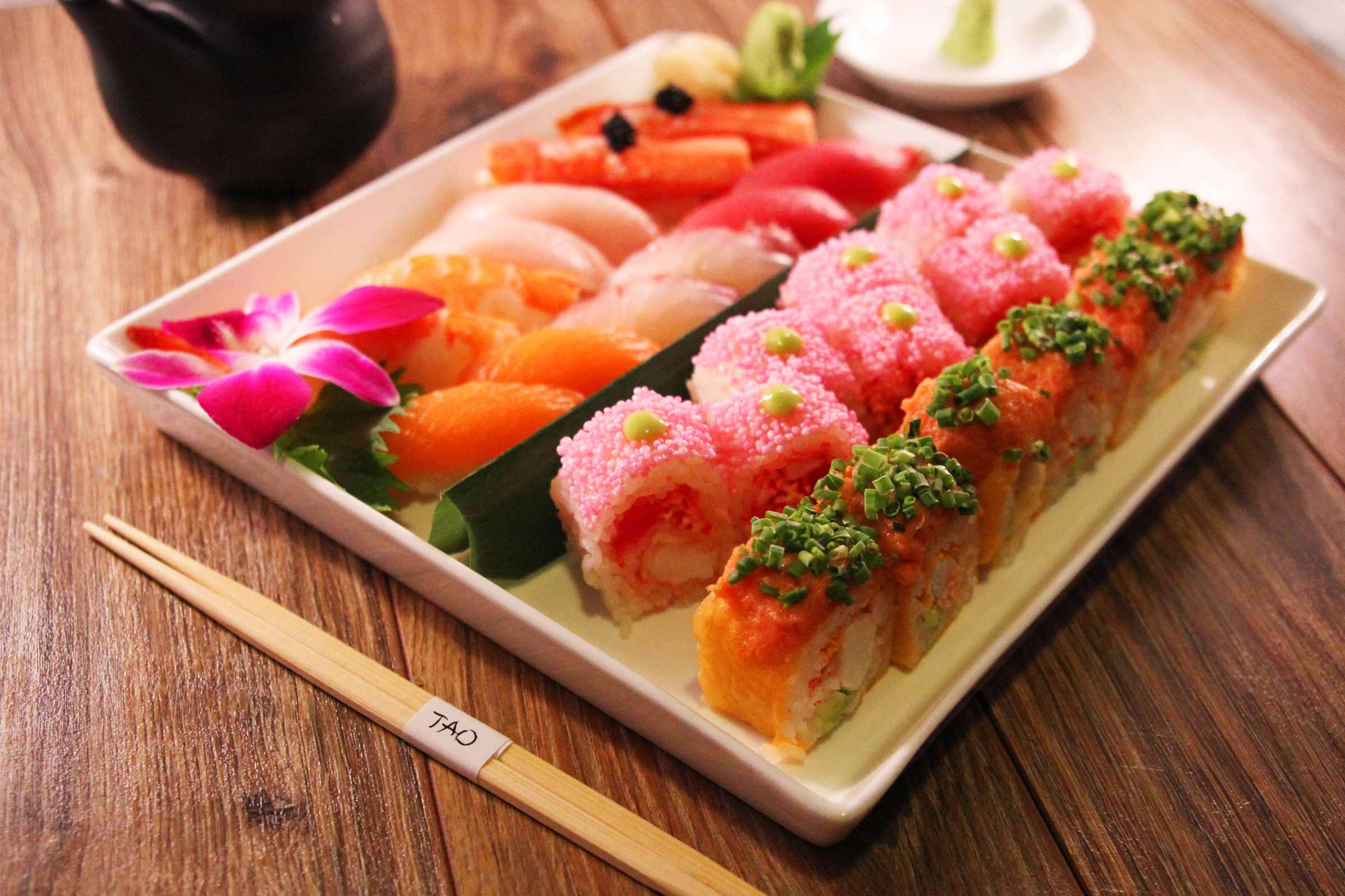 A plate of assorted sushi rolls and nigiri, garnished with flowers, served on a wooden table with chopsticks.