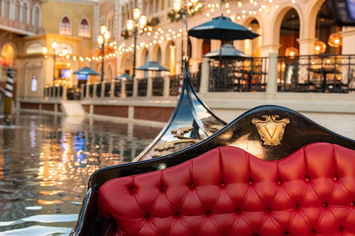 A red gondola seat on a canal with string lights and Venetian-style buildings in the background.