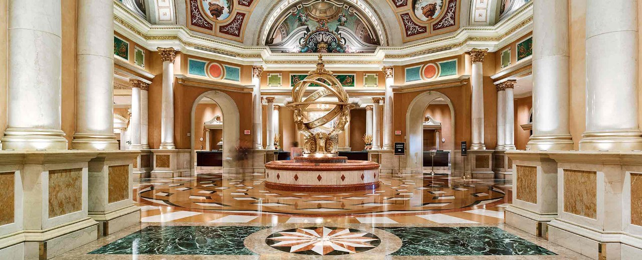 Ornate rotunda with marble columns, intricate ceiling frescoes, and a central golden statue inside a grand hall.