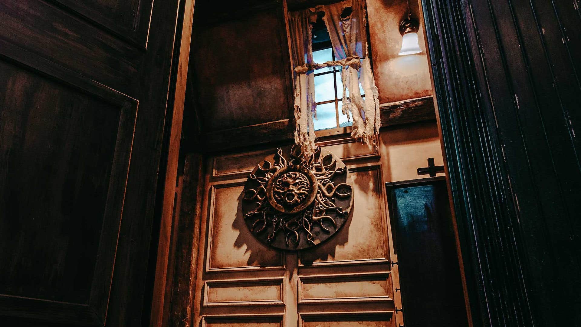 Carved wooden sun sculpture handing on an old wall with tattered curtains.