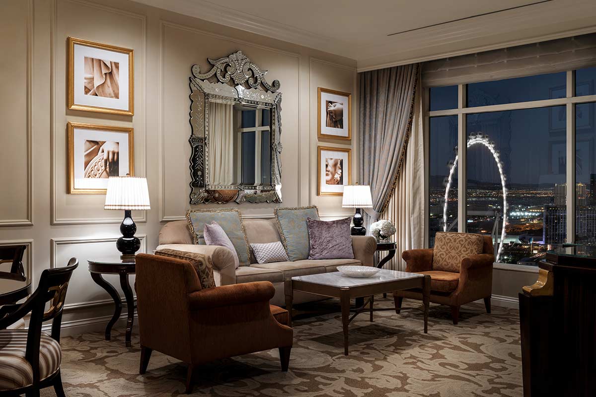 Luxurious living room with elegant furniture, ornate mirror, framed art, and large window offering a night city view.