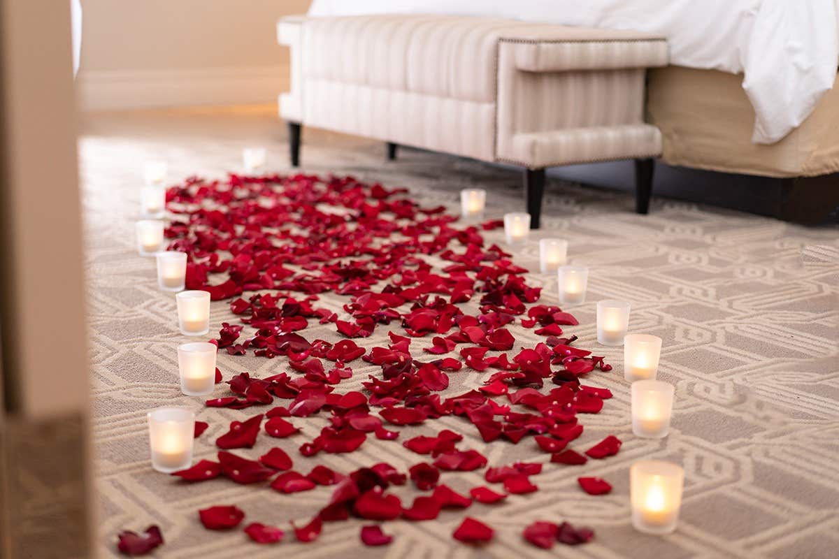 A romantic path of rose petals and candles leads to a bed in a cozy room.