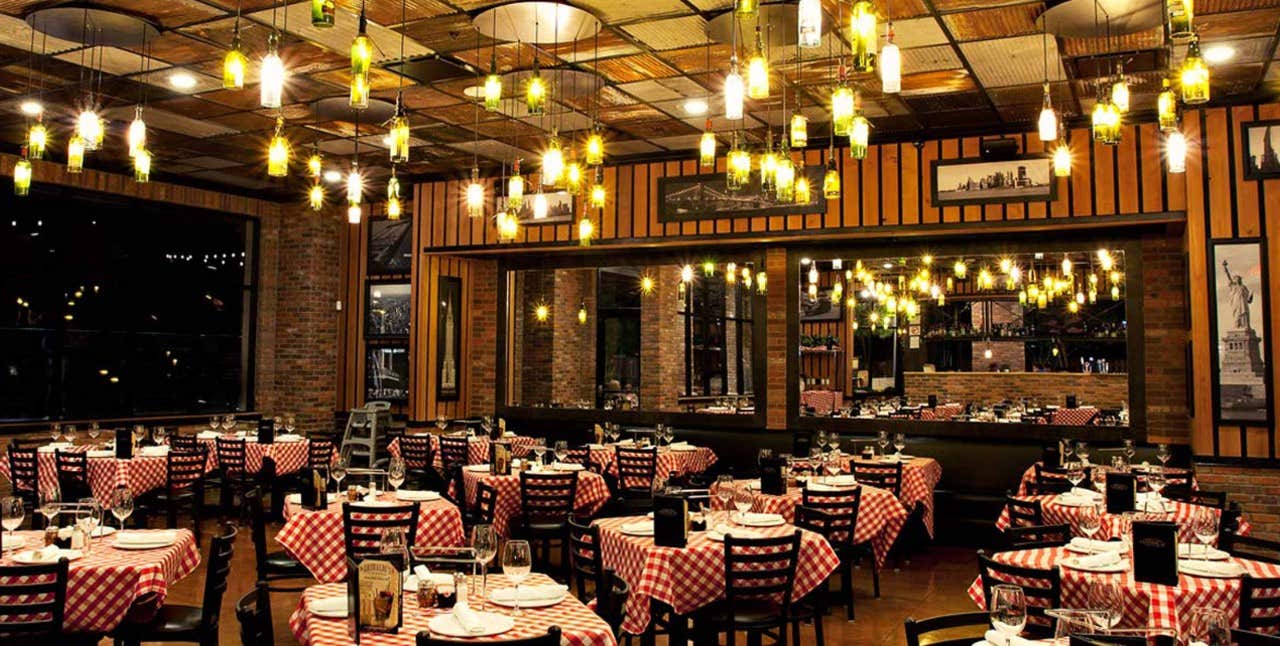 A cozy restaurant with checkered tablecloths, hanging lights, and a mirrored wall reflecting the interior.