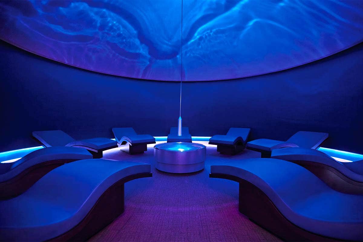 A serene spa room with curved loungers, a central round table, and calming blue ambient lighting.