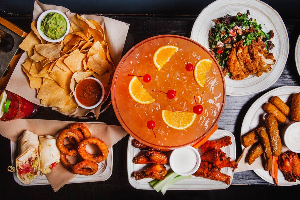 An overhead view of a table filled with a variety of dishes, including chips, dip, onion rings, chicken wings, and a large punch bowl.