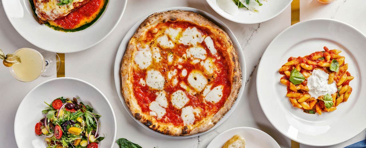 Assorted Italian dishes on a table, including a pizza, salad, pasta, and more in white plates.