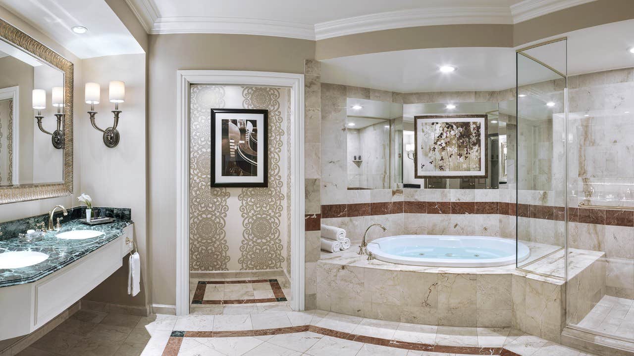 Luxurious bathroom with a marble bathtub, double sinks with mirrors, framed artwork, and elegant lighting fixtures.