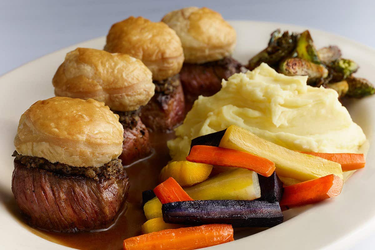 A plate with beef Wellington, mashed potatoes, roasted vegetables, and Brussels sprouts.