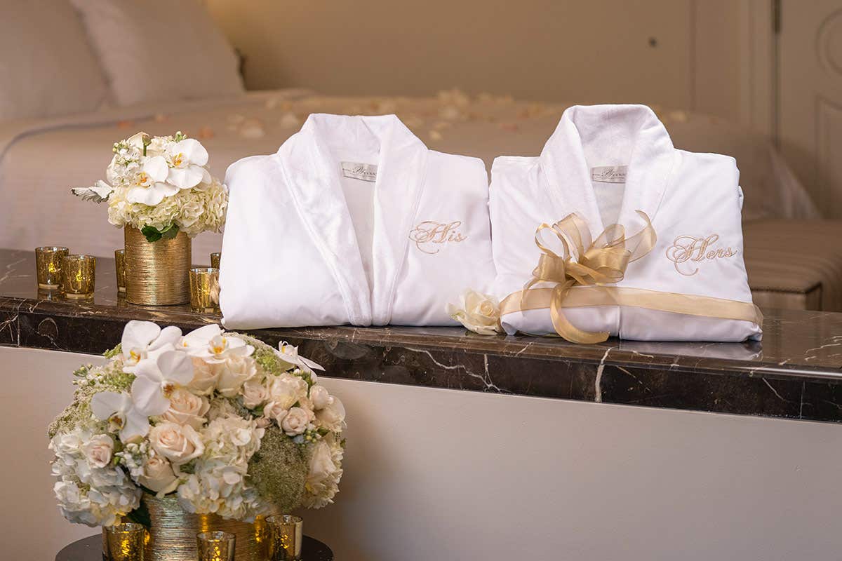 Two white robes labeled "His" and "Hers" on a marble ledge, with flower arrangements and candles nearby.