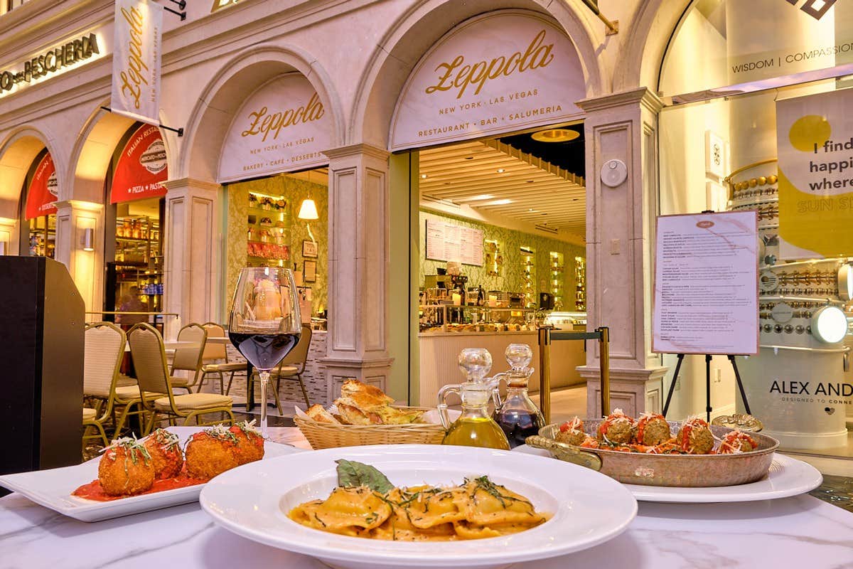 Outdoor dining area of an Italian restaurant with various dishes, including ravioli, arancini, and a glass of red wine.