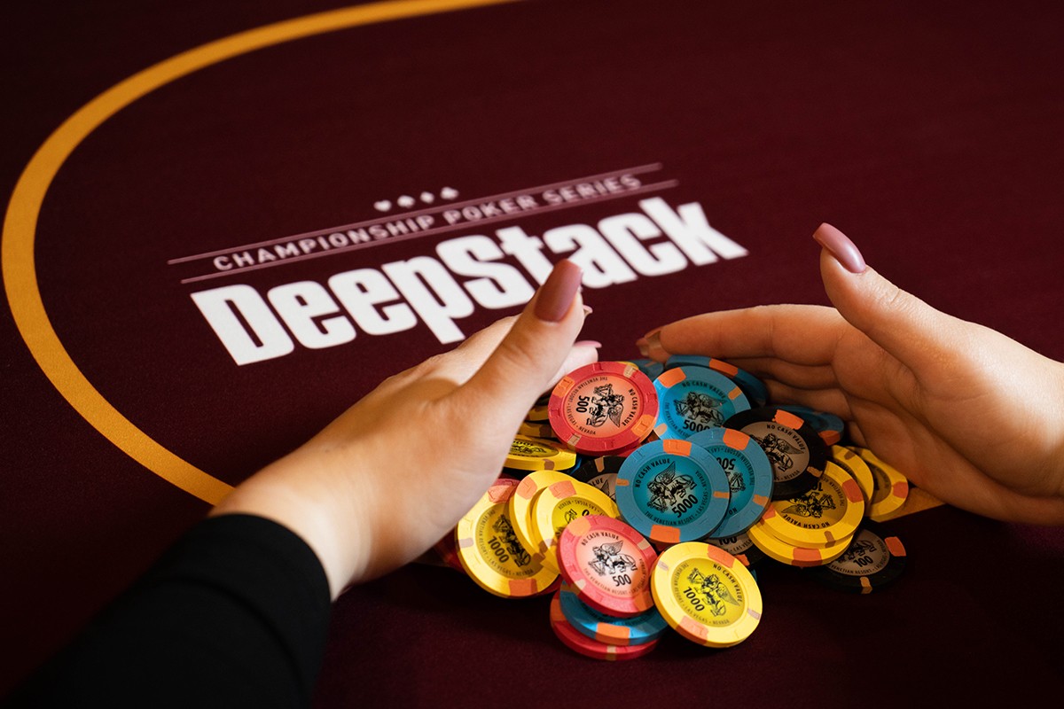 Hands reaching towards a stack of poker chips on a DeepStack Championship Poker Series table.