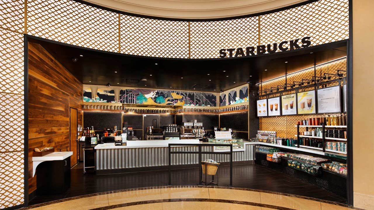 Interior view of a Starbucks coffee shop with a modern design, menu boards, and product displays behind the counter.