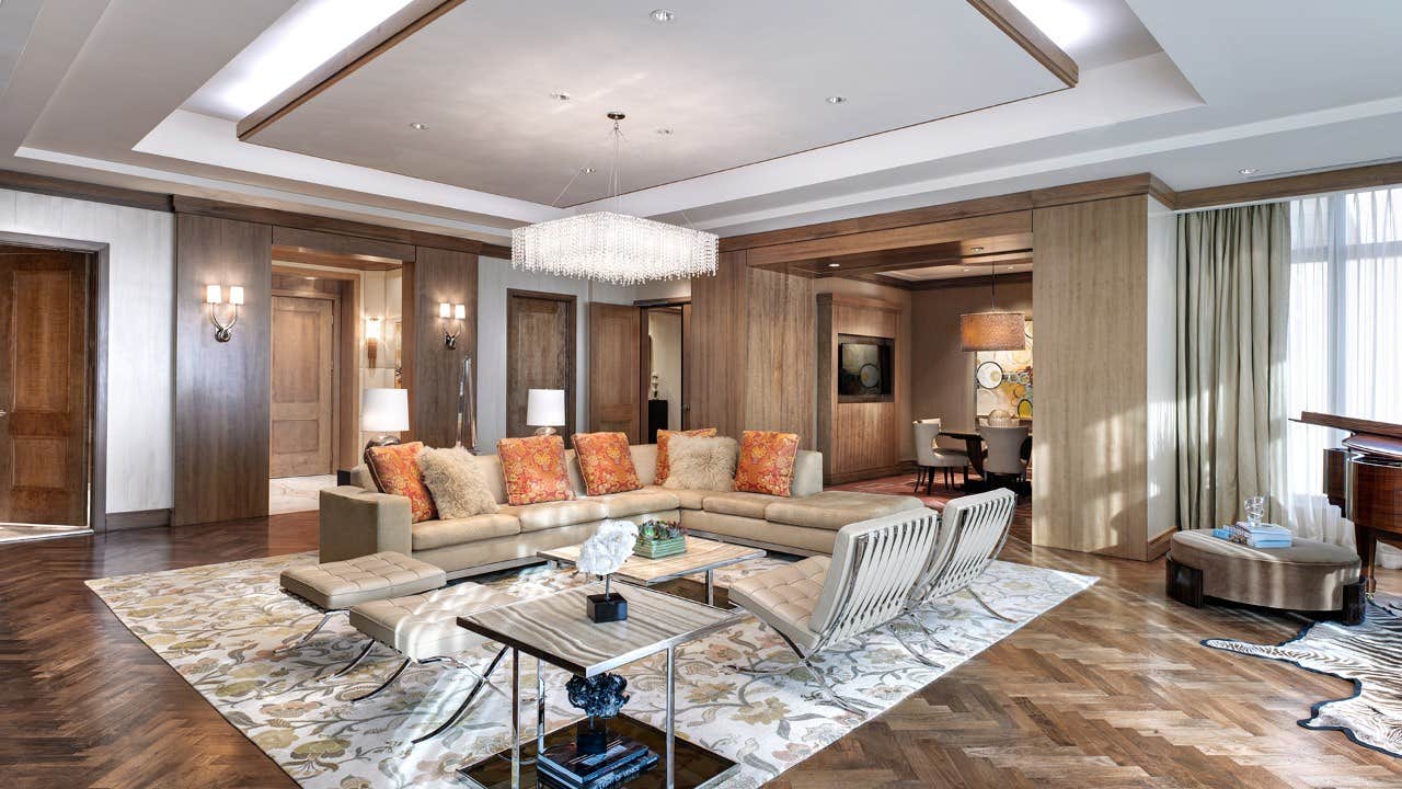 Modern living room with a beige sectional sofa, colorful pillows, a chandelier, and a grand piano in the corner.