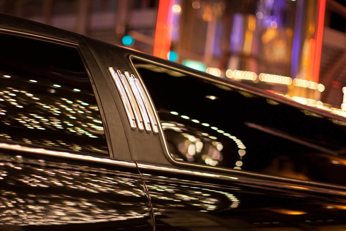 Close-up of a sleek, black limousine with illuminated city lights reflecting on its shiny surface.