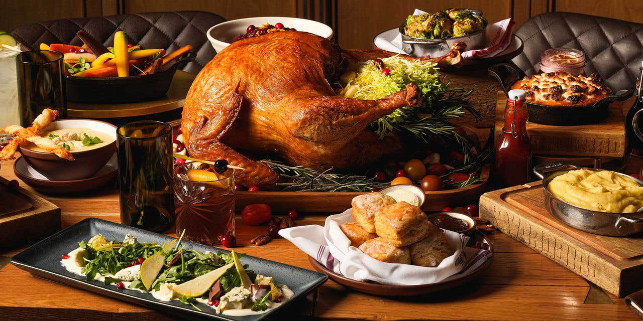 A Thanksgiving feast featuring a roasted turkey, vegetables, breads, and various side dishes on a table.