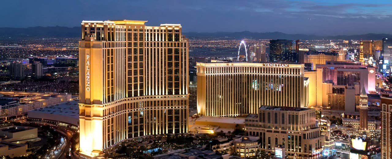 Aerial view of illuminated hotels and buildings on the Las Vegas Strip at night, with city lights in the background.