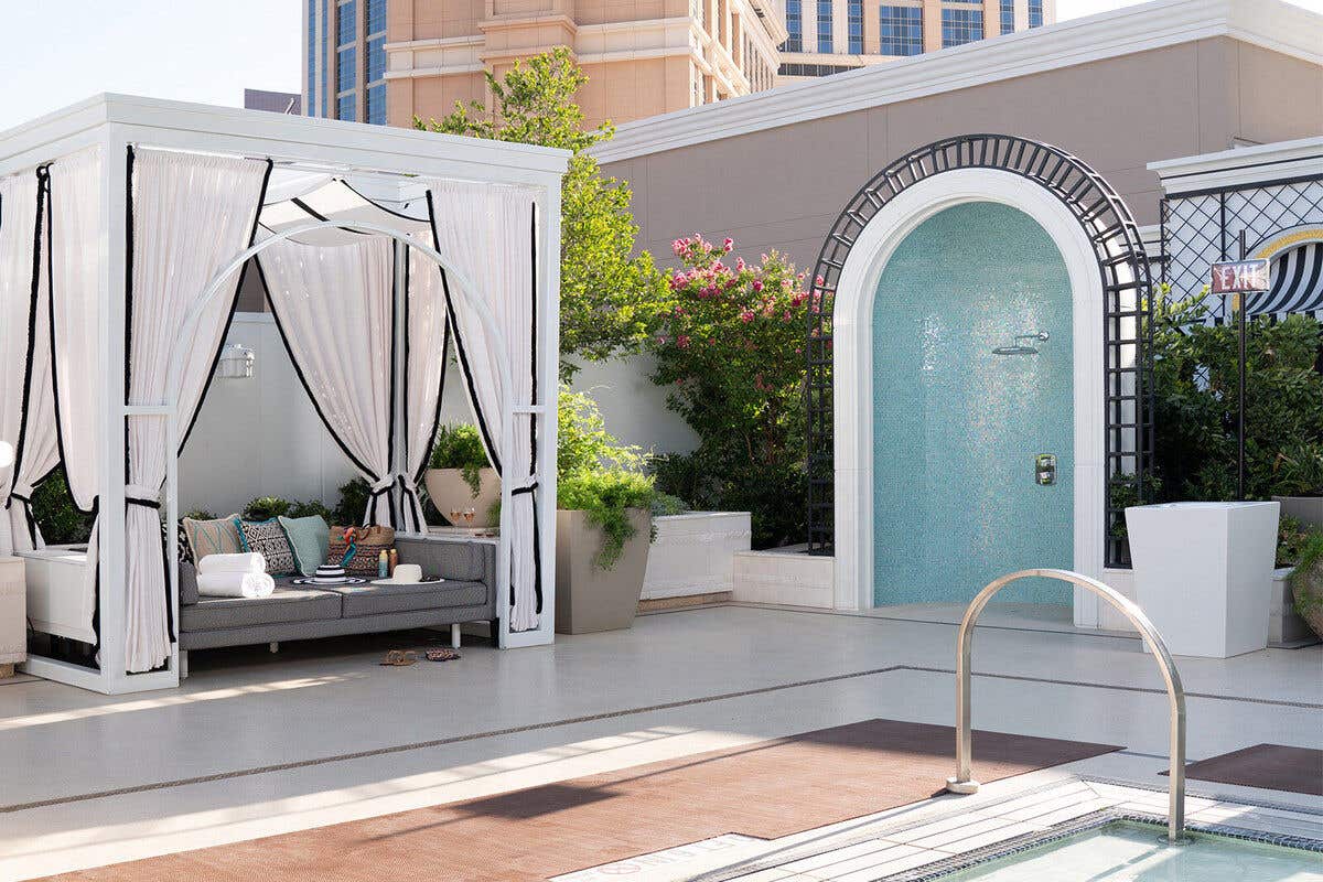 Luxurious poolside cabana with white curtains and chaise lounge chairs, set beside Palazzo tower and a sparkling pool.