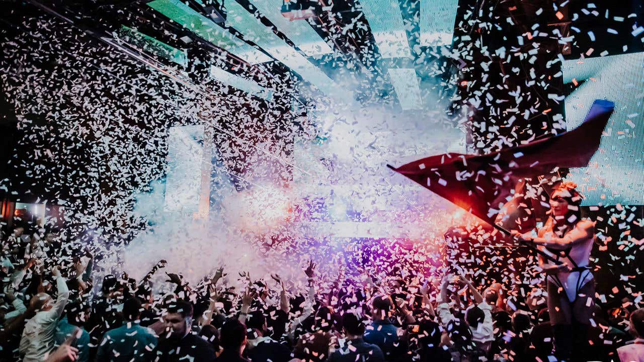 A crowded nightclub with colorful lights and beams illuminating people dancing.