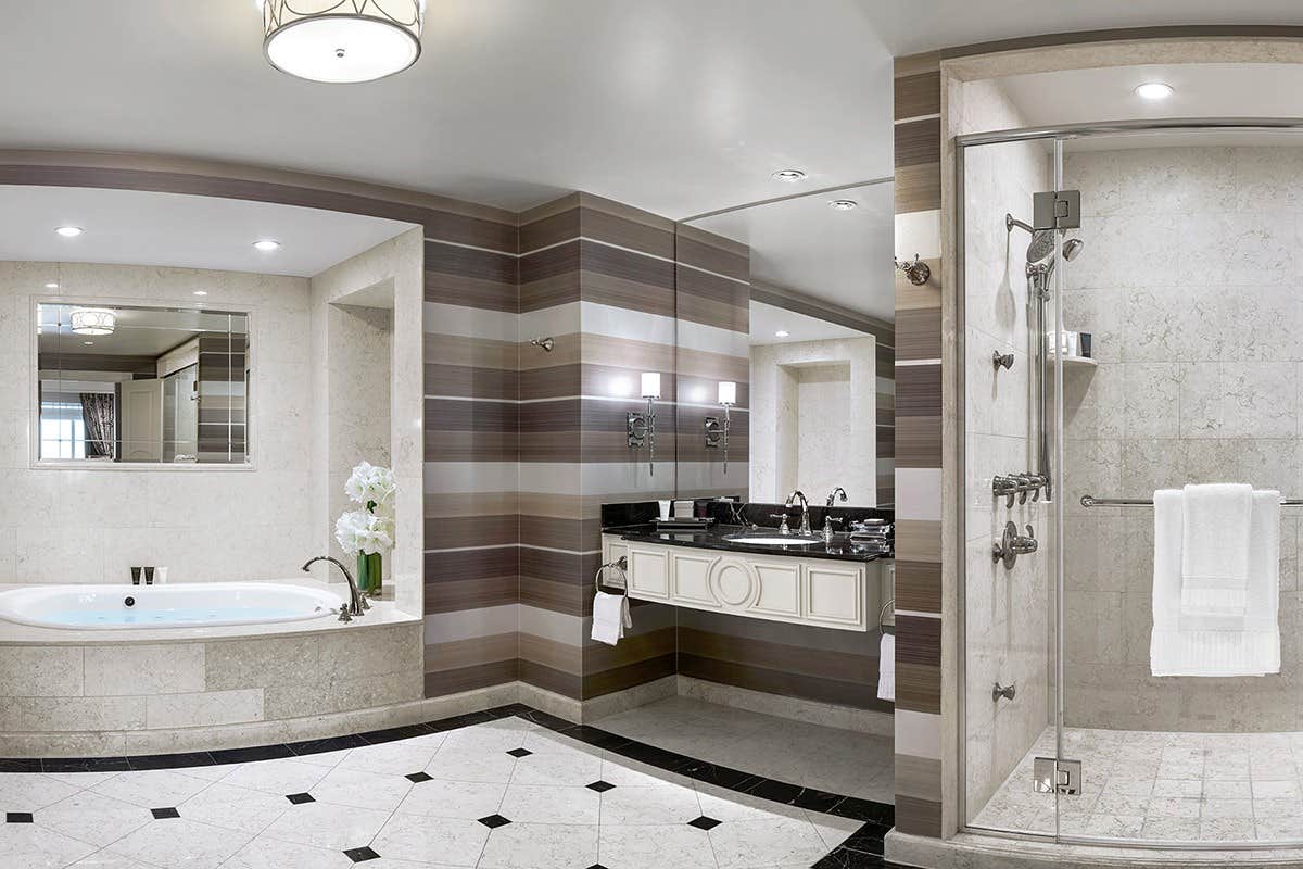 Luxurious bathroom with a marble tub, glass-enclosed shower, large mirrors, and elegant black and white flooring.