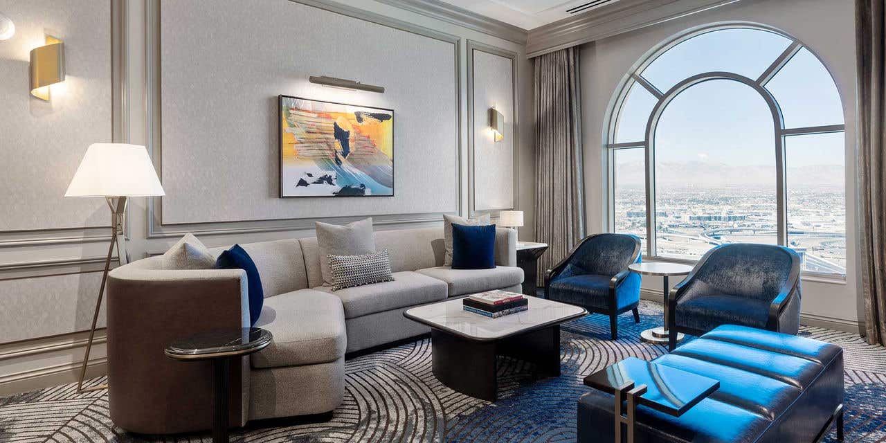 Elegant living room with a gray sofa, large arch window, blue velvet chairs, and abstract wall art.