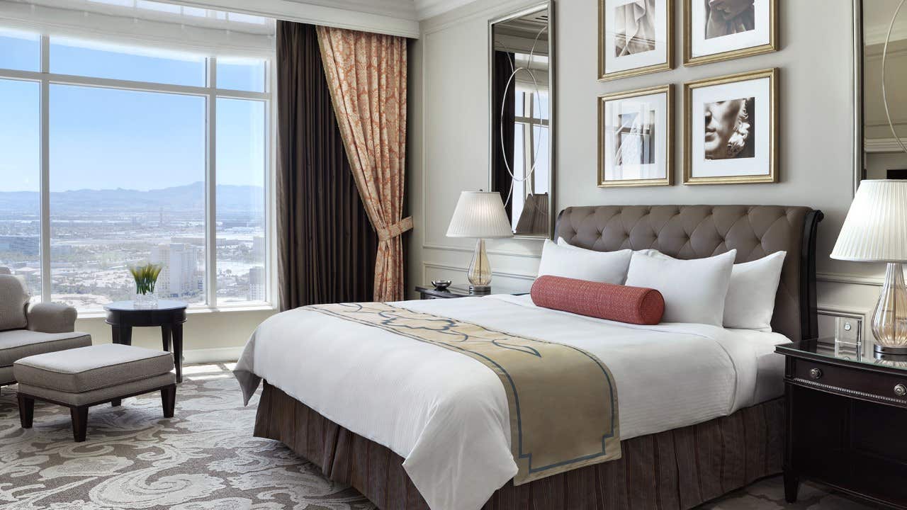 Luxurious hotel room with a large bed, elegant décor, large windows offering city views, and a cozy seating area.