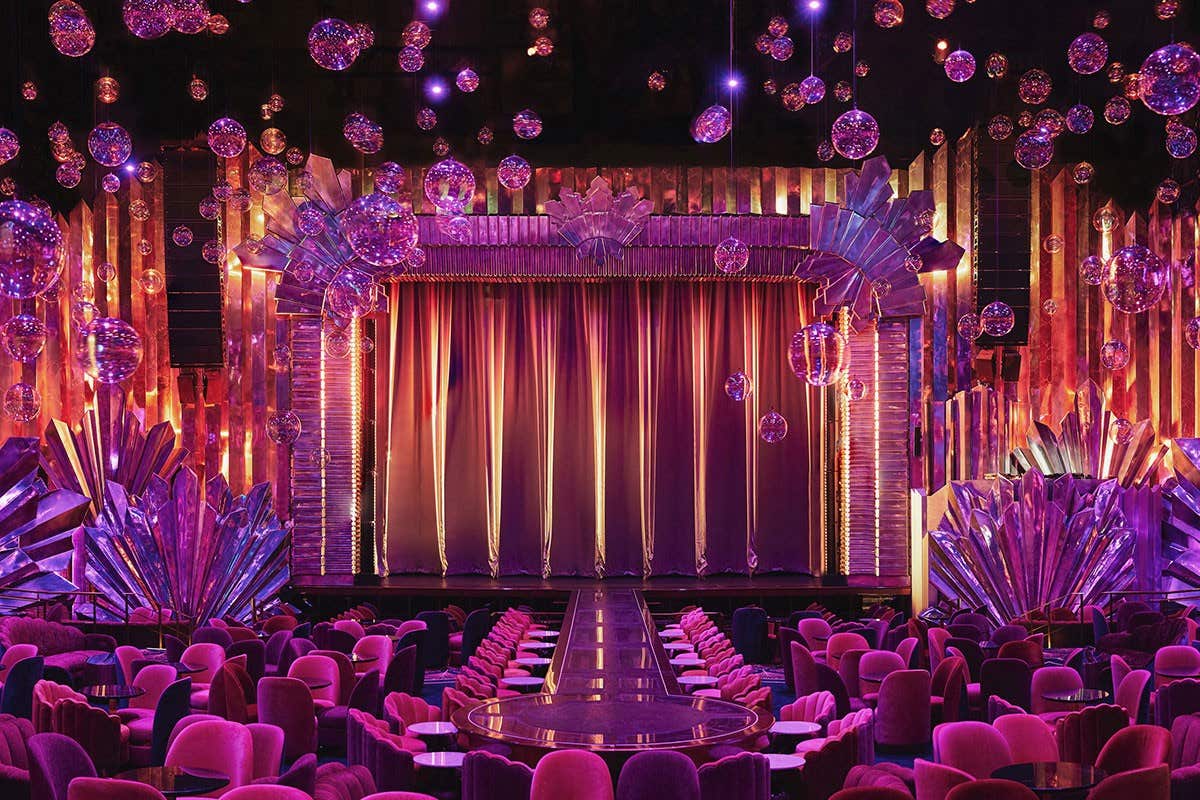 A vibrant theater stage with luxurious pink and purple decor, featuring hanging lamps and an elegant curtain.