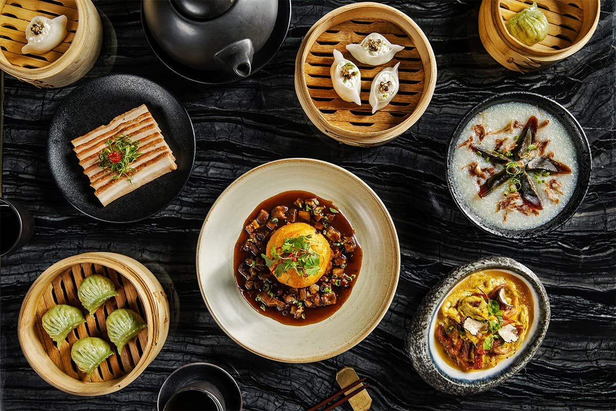 A variety of Chinese dishes, including dim sum, steamed buns, dumplings, and vegetable dishes on a marble table.