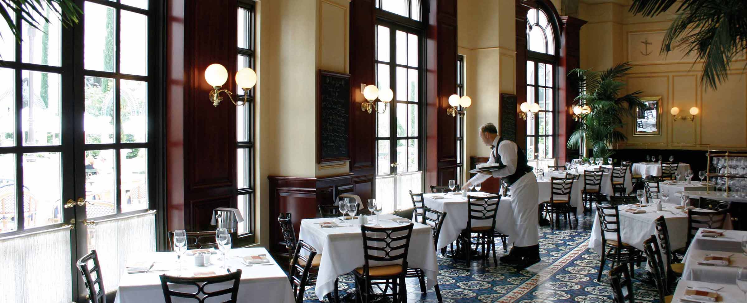 Elegantly appointed restaurant with large windows, white tablecloths, and a waiter serving a table.