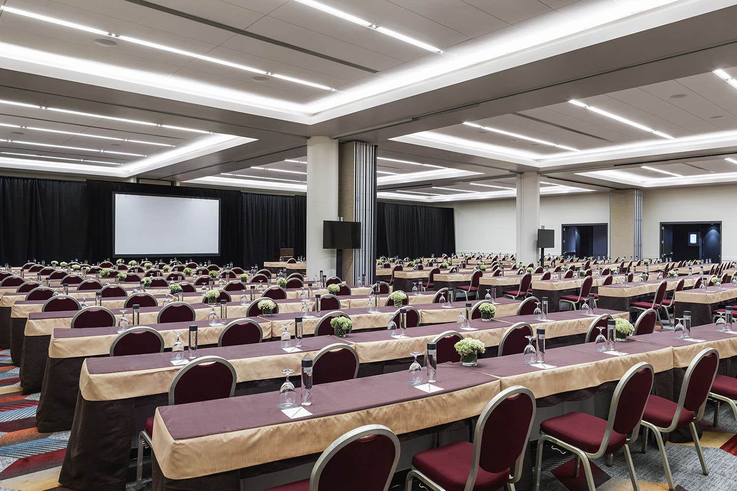 The inside of a meeting room at the Venetian Resort with rows of tables set up for an event, a TV, and a projector screen. 