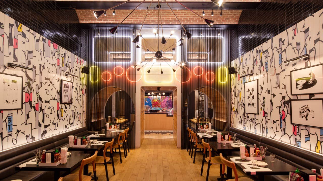 A modern restaurant with colorful wall art, hanging lights, and neatly arranged tables and chairs.