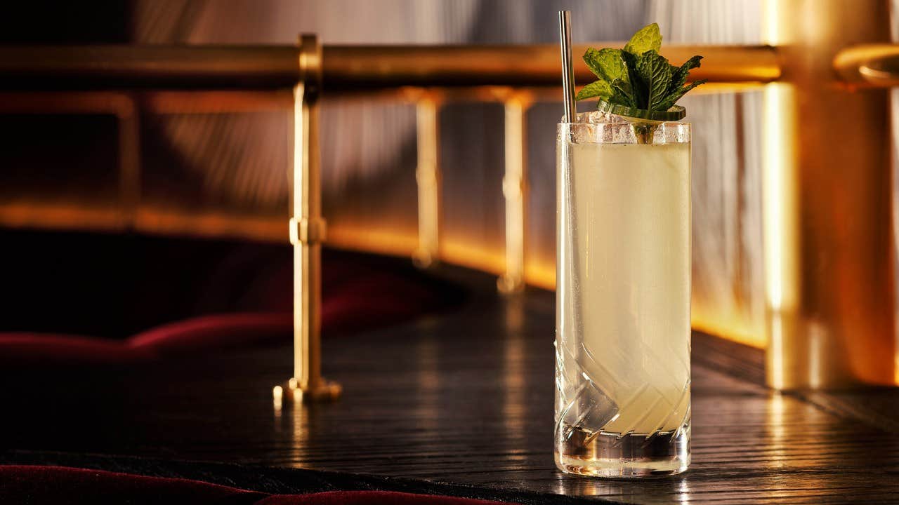 Tall glass of a light-colored cocktail garnished with fresh mint leaves, set on a dark, elegant bar counter.