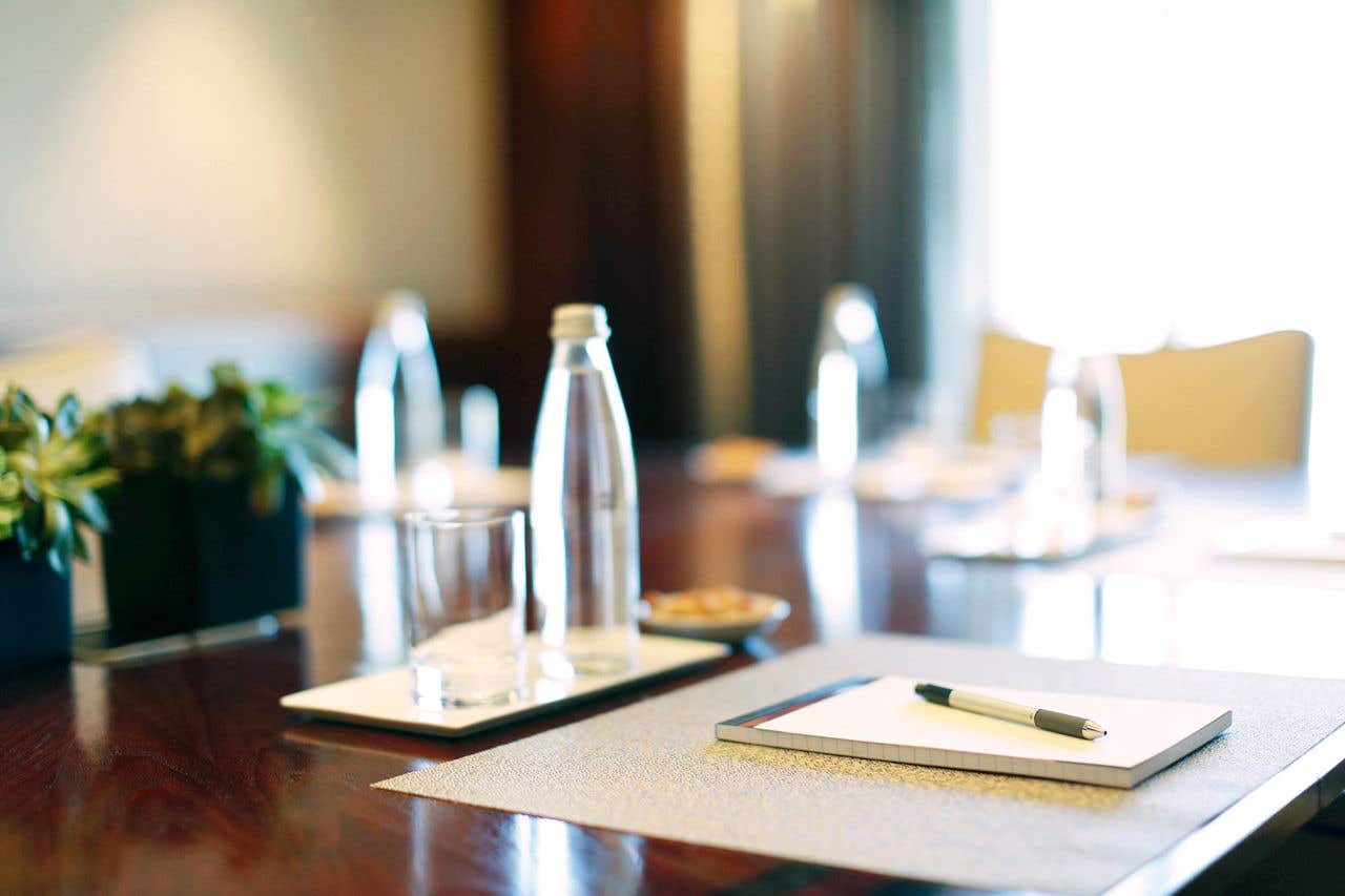 a close up image of a water bottle, a glass, and snacks on a table with a pad of paper and pen