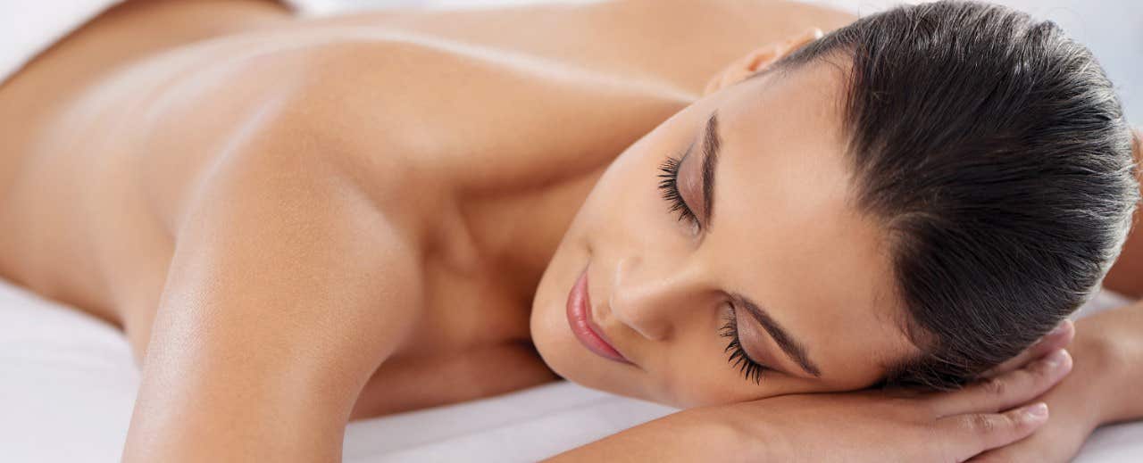 Woman with a peaceful expression lying on her stomach with eyes closed, possibly receiving a massage.