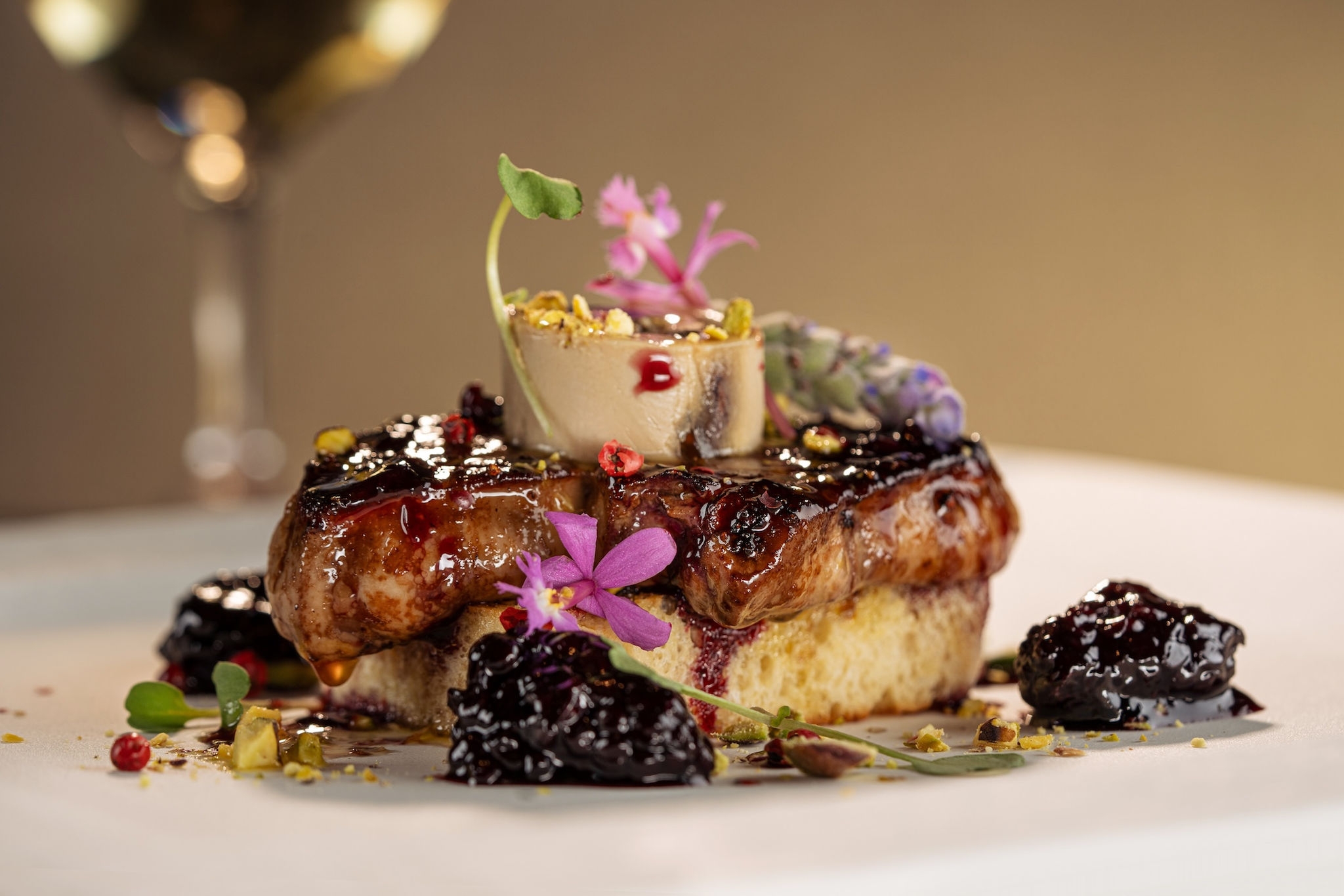 A decadent pastry dish with sauce, cooked black berries garnished with delicate flowers.