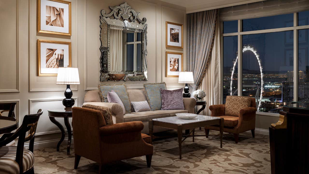 Elegant living room with sofas, armchairs, a large mirror, wall art, and a nighttime city view through a window.