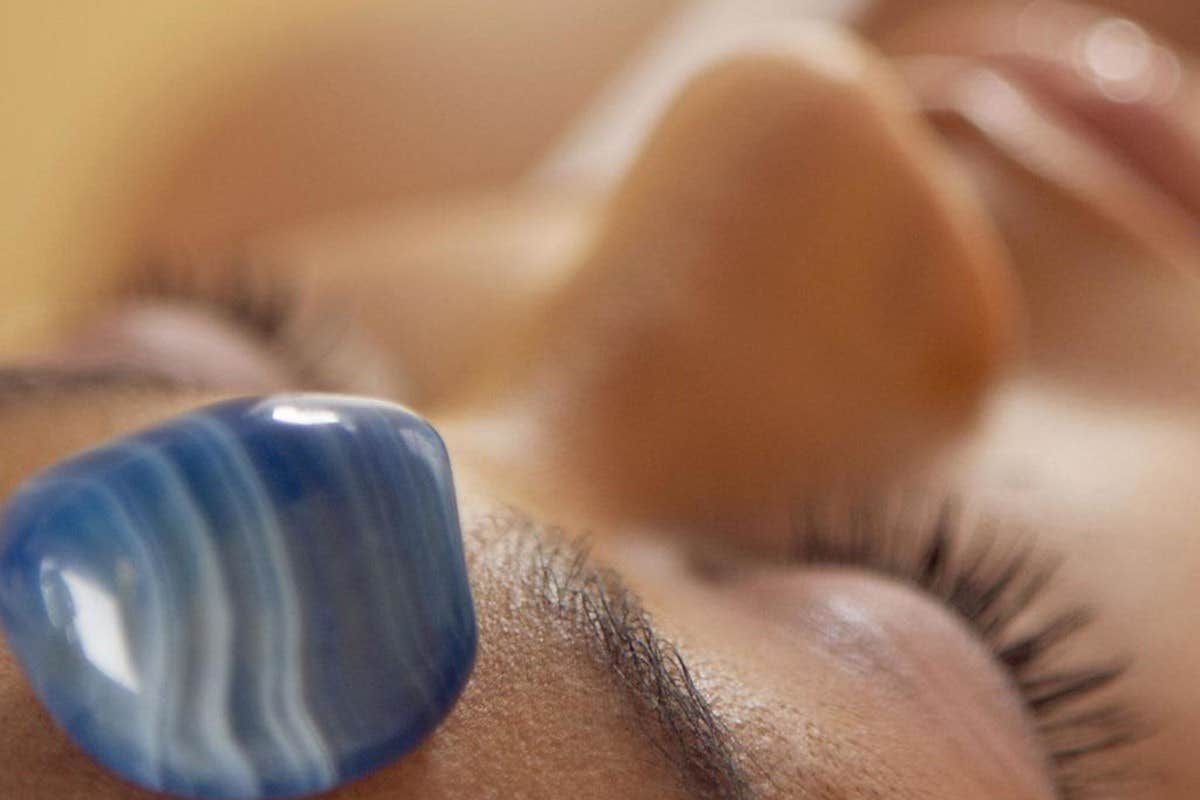 Close-up of a person with a blue polished stone placed on their forehead and eyes closed.