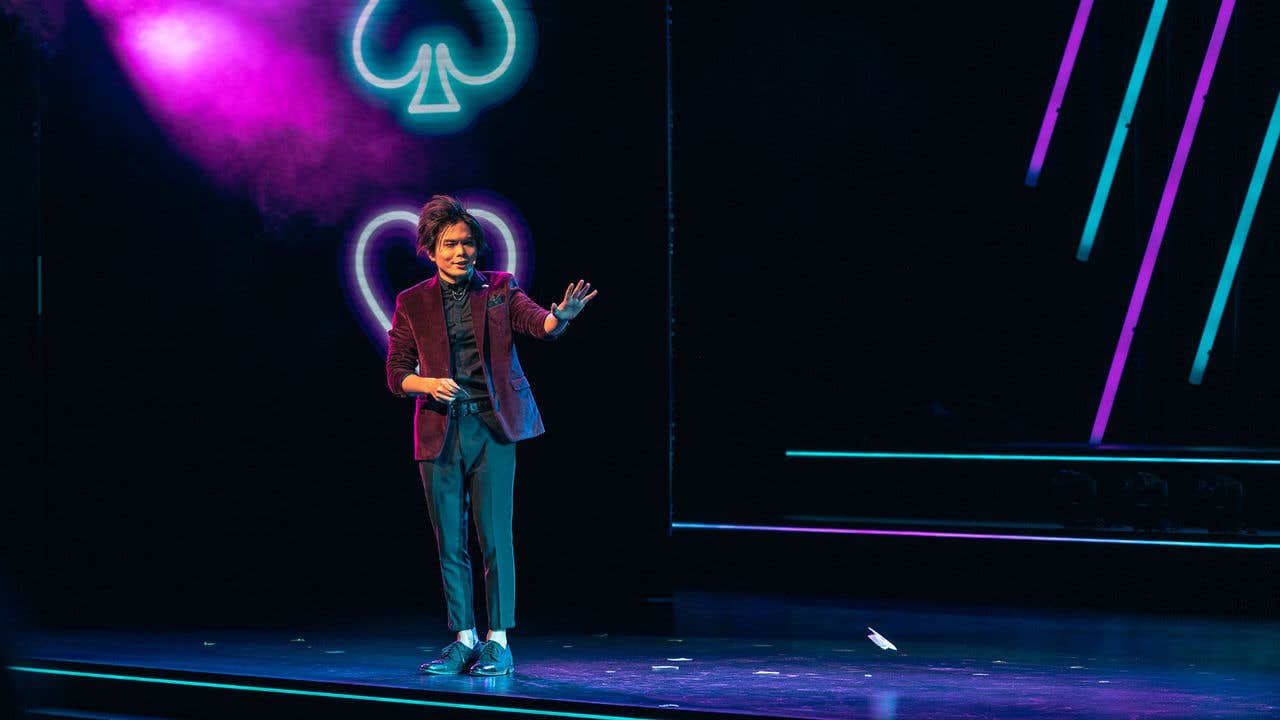 Shin Lim on stage with neon lighting and a spade symbol in the background.