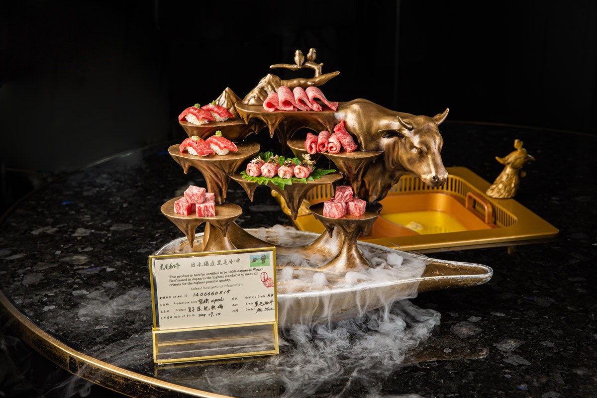 A detailed meat platter with numerous cuts arranged on an artistic bull sculpture with mist effect and a menu card.