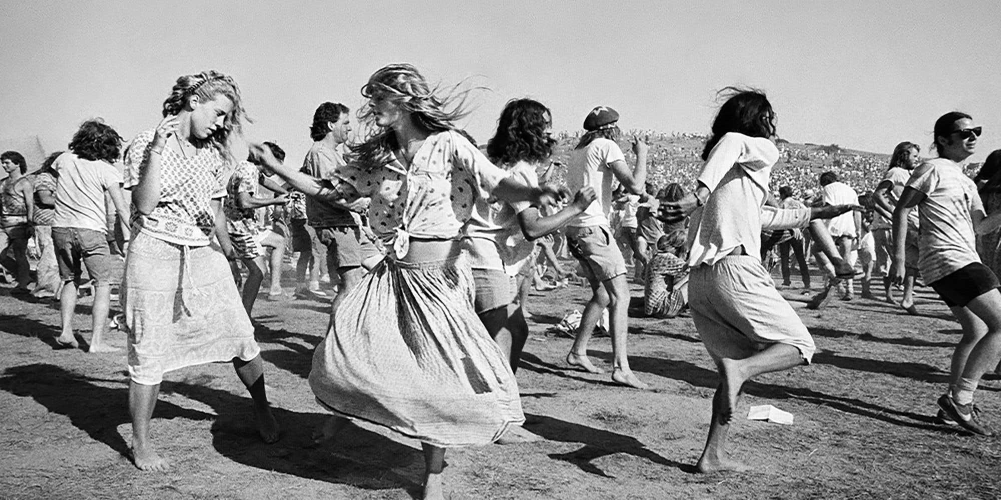 A black and white photo of a group of people dancing outdoors in a large open field