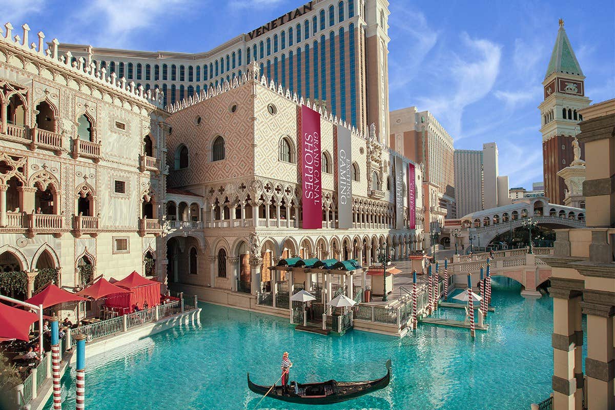 Gondola on blue water at The Venetian, Las Vegas, with Italian-inspired architecture and shopping banners.