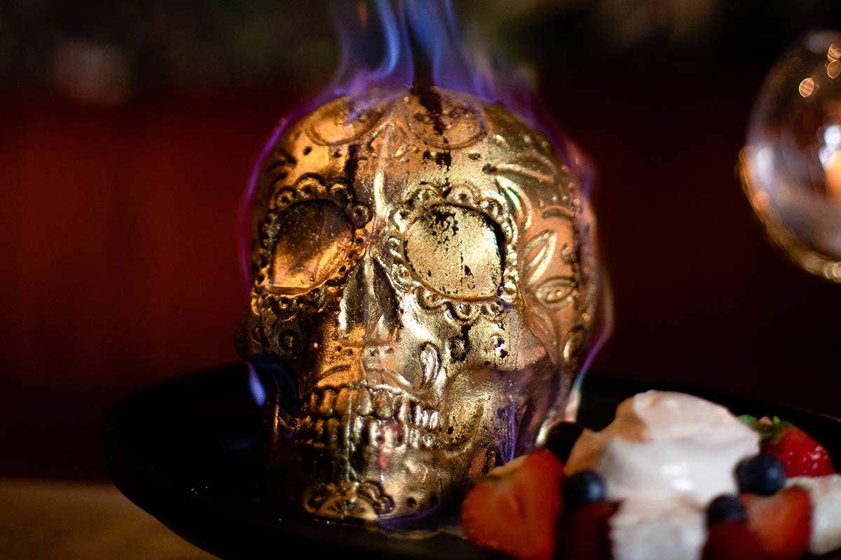 A decorated golden skull with purple flames on top, placed next to a dessert with whipped cream and berries.