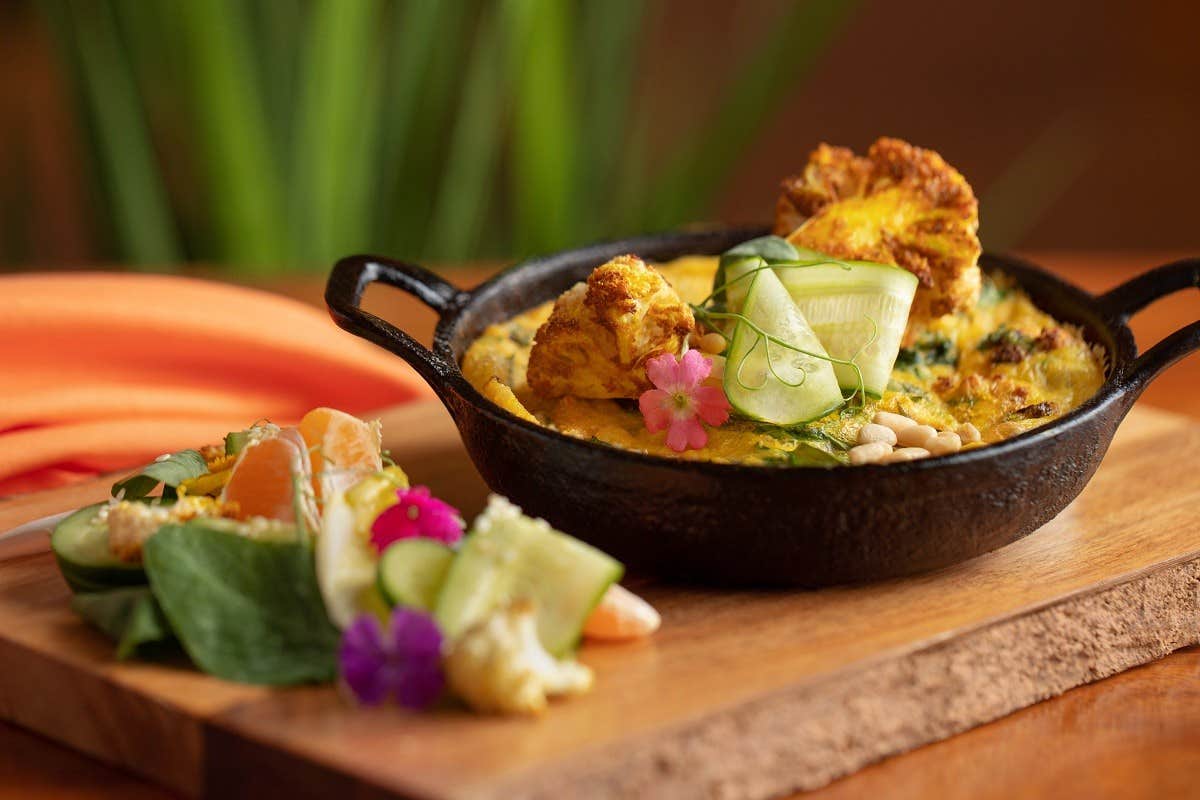 A vibrant vegetarian dish in a cast-iron skillet with a fresh salad on a wooden board, decorated with edible flowers.