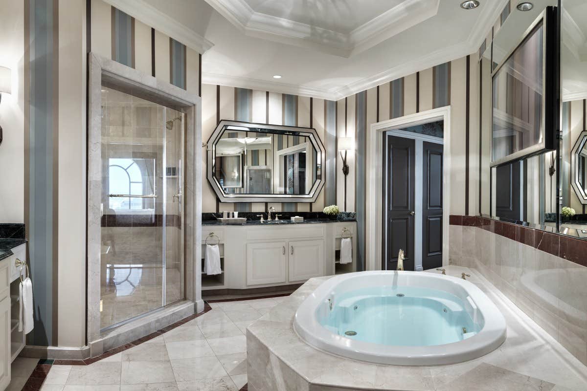 Luxurious bathroom with a soaking tub, glass shower, dual sinks, striped walls, and elegant lighting fixtures.