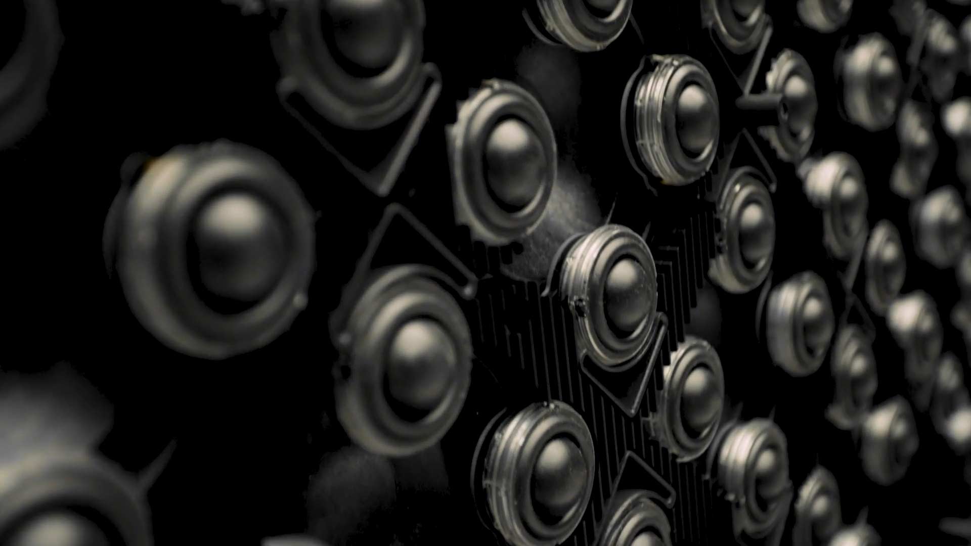 Close-up view of numerous black circular speakers arranged in dense pattern, creating a textured surface.