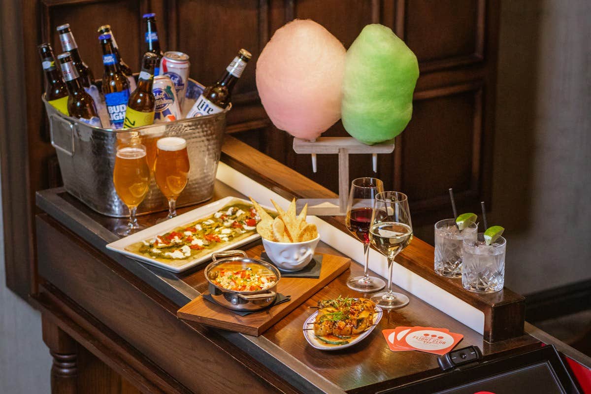 A table with beers on ice, cocktails, wine, cotton candy, and a variety of appetizers including chips and dips.