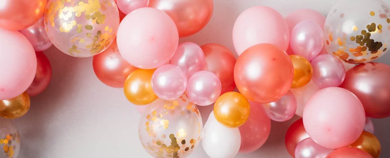 Decorative balloons in shades of pink, orange, and white with gold confetti inside some of the clear balloons.