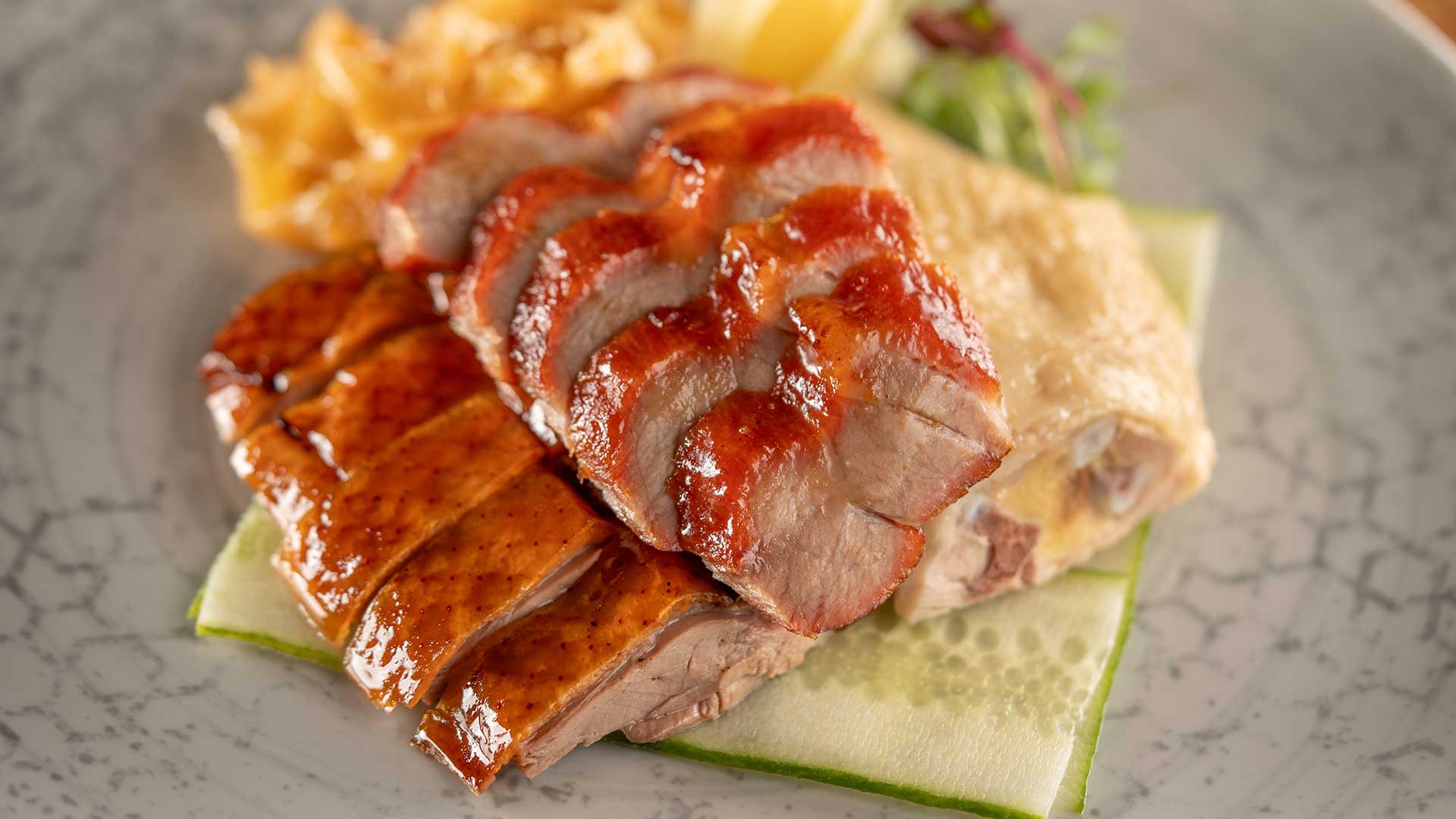 Close-up of a plate with sliced roasted duck, pasta, and vegetables, presented on a decorative grey dish.