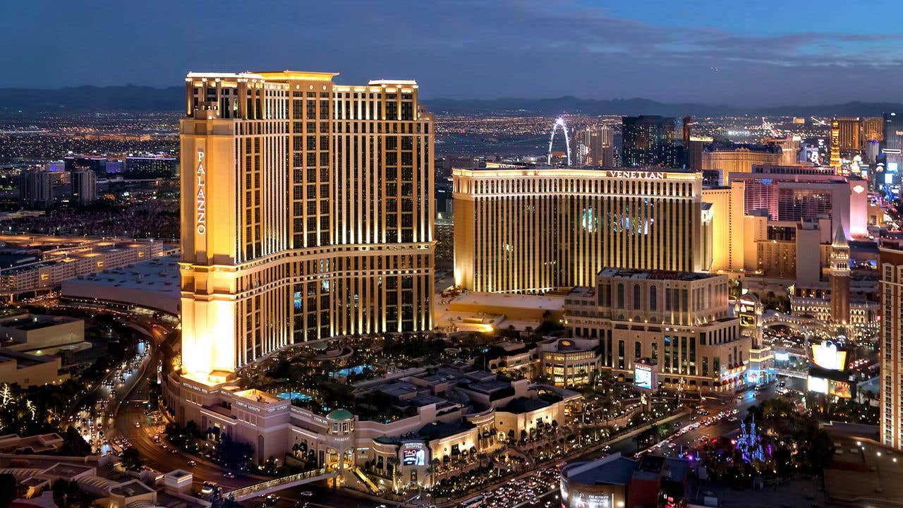 Aerial view of illuminated Las Vegas Strip at dusk, featuring high-rise hotels, casinos, and city lights.