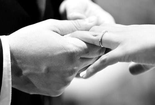 Close-up of one hand placing a ring on another hand's finger, symbolizing a wedding or engagement ceremony.